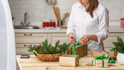 Merry Christmas and Happy Holidays. A woman is packing gifts, tying ribbons on boxes at the table at home. Preparing for the holidays. Top view