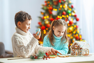 Close-up, children hold a handmade Christmas gingerbread house decorated with sweets in the shape...