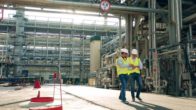 Pipelines of the oil-processing plant with two inspectors passing by