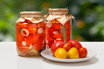 Pickled tomatoes in glass jars on natural background.