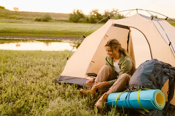 Abwaschbare Fototapete Camping Weiße Frau, die ihre Schnürsenkel bindet, während sie beim Camping im Zelt sitzt