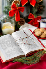 reading, winter holidays and leisure concept - close up of open book with glasses, fir branch, cookies and christmas decorations on window sill at home