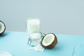Coconut products. Cracked open coconut with meat cut in half, coconut powder in a glass jar, plant milk on a blue background. isometric projection. Copy space. Concept alternative milk, vegeterian