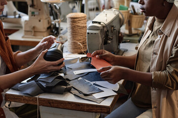 Close-up of two tailors sitting at the table and repairing shoes from pieces of leather in the...