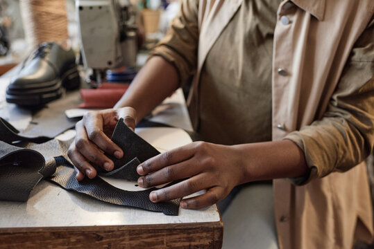 Close-up of tailor sitting at the table and examining the pieces of leather during her work in the workshop