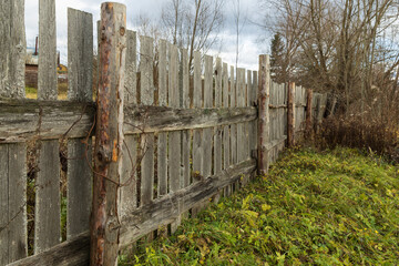 Wooden plank palisade separating the land plot with a field and shrubbery