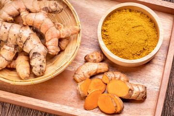 TurmTurmeric Powder and Turmeric root in wooden plate, Curry Powder on a wooden table background.