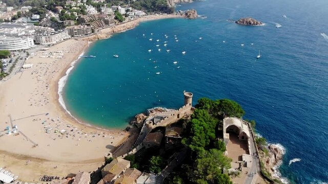 Drone view of the fortress with scenic sea views in Tossa de Mar. Drone shot of a municipality in Spain. People are relaxing on a sandy beach in Spain. Spa town near the Mediterranean Sea