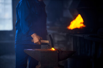 Close up of blacksmith hands hitting with hammer on glowing hot metal. Man processing metal on...