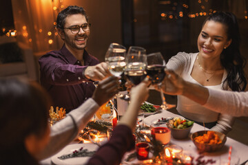 holidays, party and celebration concept - multiethnic group of happy friends having christmas dinner at home and drinking wine