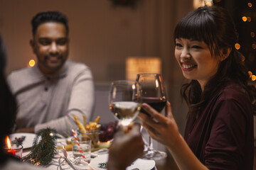 holidays, party and celebration concept - multiethnic group of happy friends having christmas dinner at home and drinking wine