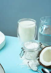 Coconut products. Cracked open coconut with meat cut in half, coconut powder in a glass jar, plant milk on a blue background. isometric projection. Copy space. Concept alternative milk, vegeterian