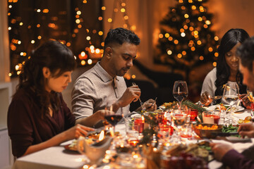 holidays, party and celebration concept - multiethnic group of happy friends having christmas dinner at home