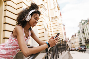 Black woman in headphones smiling while using mobile phone