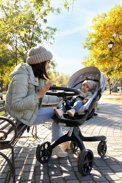Happy mother with her baby son in stroller outdoors on autumn day