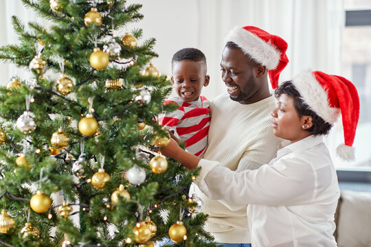 family, winter holidays and people concept - happy african american mother, father and little son decorating christmas tree at home on