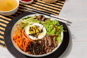 bibimbap or pibimpap, one of the most popular dishes of Korean cuisine. Boiled rice with various salads and egg. Serving with broth and sauce on a bamboo napkin, close-up