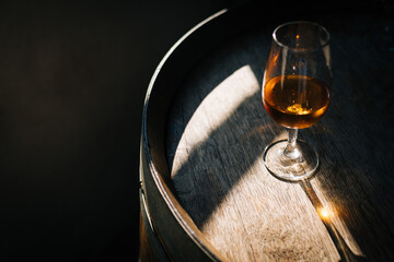 Glass of Porto wine on a wooden oak barrel with long shadow in moody atmosphere 
