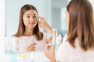 health, vision and old people concept - teenage girl applying contact lenses in front of mirror at...