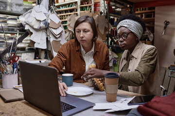 Two dressmakers sitting at the table and working on laptop in team they developing new project of clothes together in the workshop