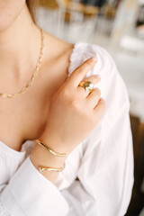 Woman's hand lies on a white shirt demonstrating gold jewelry