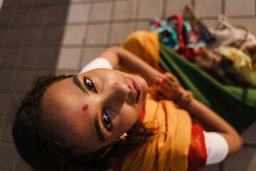 Young indian woman making namaste gesture while sitting on sidewalk