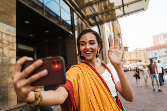 Young indian woman wearing sari taking selfie on cellphone at city street