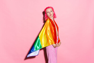 Shirtless woman looking at camera while posing with rainbow flag