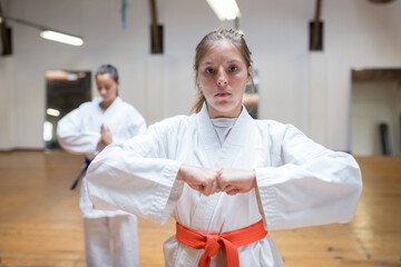 Inspired young women at karate training. Attractive women in white clothes with blue and red belts warming up before training. Sport, healthy lifestyle concept