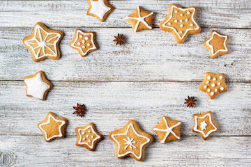 Frame of Christmas gingerbreads in the shape of a star with patterns of glaze and spices on a white wooden background.