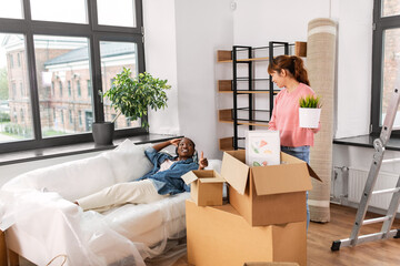 moving, people and real estate concept - happy smiling woman unpacking box and her friend resting...