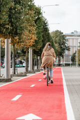 traffic, city transport and people concept - woman riding bicycle along red bike lane or two way road on street