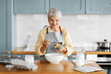 people and culinary concept - happy smiling woman cooking food on kitchen at home and adding butter - obrazy, fototapety, plakaty