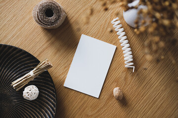 Autumn wedding invitation card mockup. Still life with blank paper card, vase of dried flax, ribbon, plate, autumn decorations.