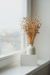 Blank paper card and vase with dried flax flowers on windowsill. Nordic style living room interior...