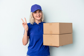 Young delivery caucasian woman isolated on blue background joyful and carefree showing a peace symbol with fingers.