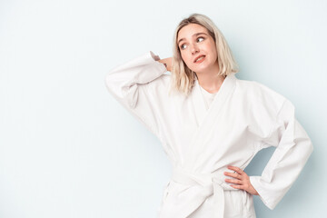 Young caucasian woman doing karate isolated on blue background touching back of head, thinking and making a choice.