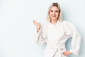 Young caucasian woman doing karate isolated on blue background showing a copy space on a palm and holding another hand on waist.