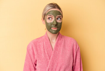 Young caucasian woman wearing face mask isolated on yellow background confused, feels doubtful and unsure.