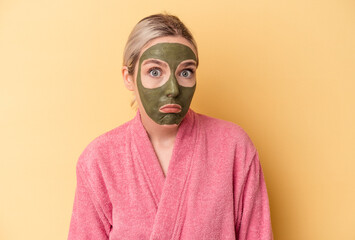 Young caucasian woman wearing face mask isolated on yellow background shrugs shoulders and open eyes confused.