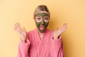 Young caucasian woman wearing face mask isolated on yellow background receiving a pleasant surprise, excited and raising hands.