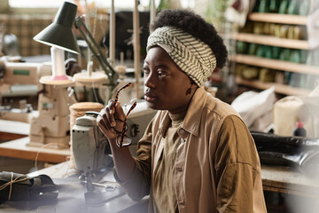 Pensive seamstress sitting at her workplace with sewing machine, she making little break between work