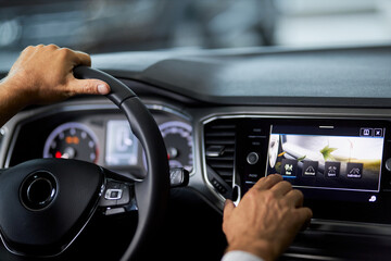 Close up of man touching multimedia screen of luxury car while sitting inside. Male customer testing modern innovative dashboard before buying vehicle. Selling and purchase concept. - obrazy, fototapety, plakaty