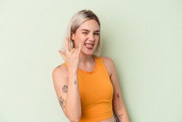 Young caucasian woman isolated on green background showing rock gesture with fingers