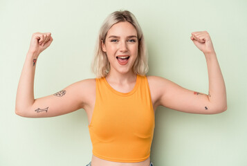 Fototapeta premium Young caucasian woman isolated on green background showing strength gesture with arms, symbol of feminine power