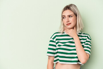 Young caucasian woman isolated on green background touching back of head, thinking and making a choice.