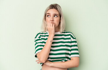 Young caucasian woman isolated on green background biting fingernails, nervous and very anxious.