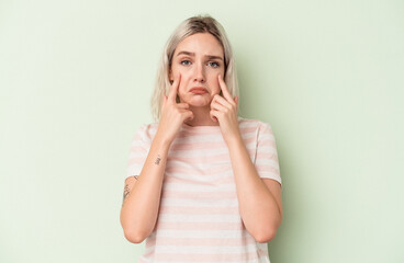 Young caucasian woman isolated on green background crying, unhappy with something, agony and confusion concept.