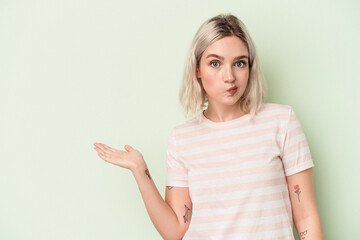 Young caucasian woman isolated on green background showing a copy space on a palm and holding another hand on waist.