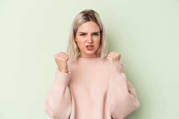 Young caucasian woman isolated on green background showing fist to camera, aggressive facial expression.